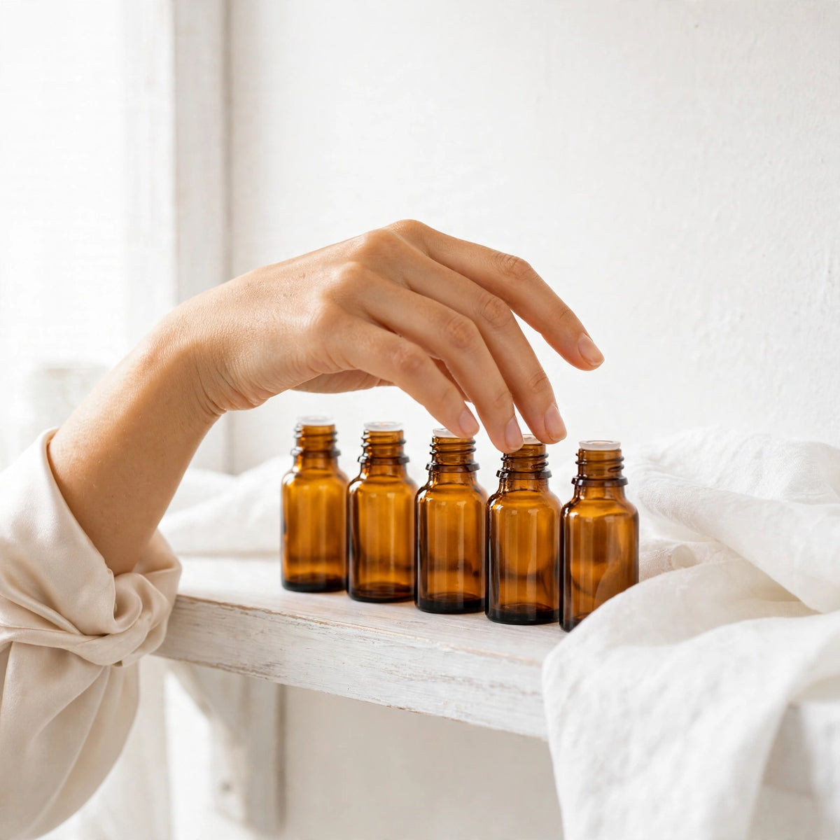 Fingertips along small amber bottles of YNA Parfums extrait de parfum aged before bottling