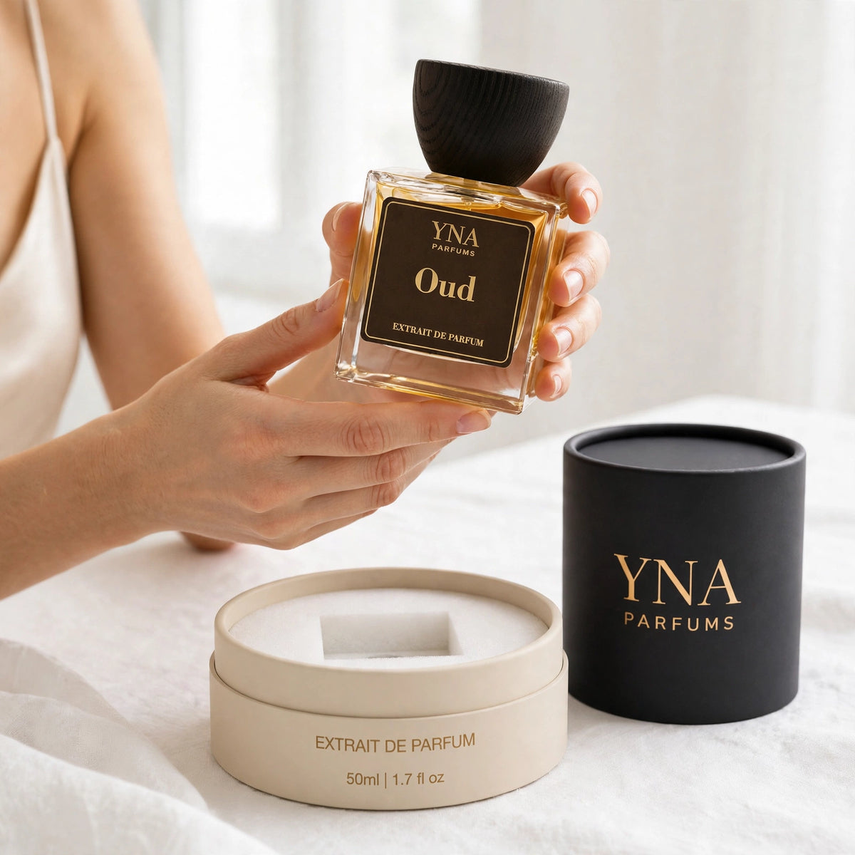 Hands lifting YNA Parfums Oud Extrait de Parfum 50ml out of its cylinder tube box with white foam padding